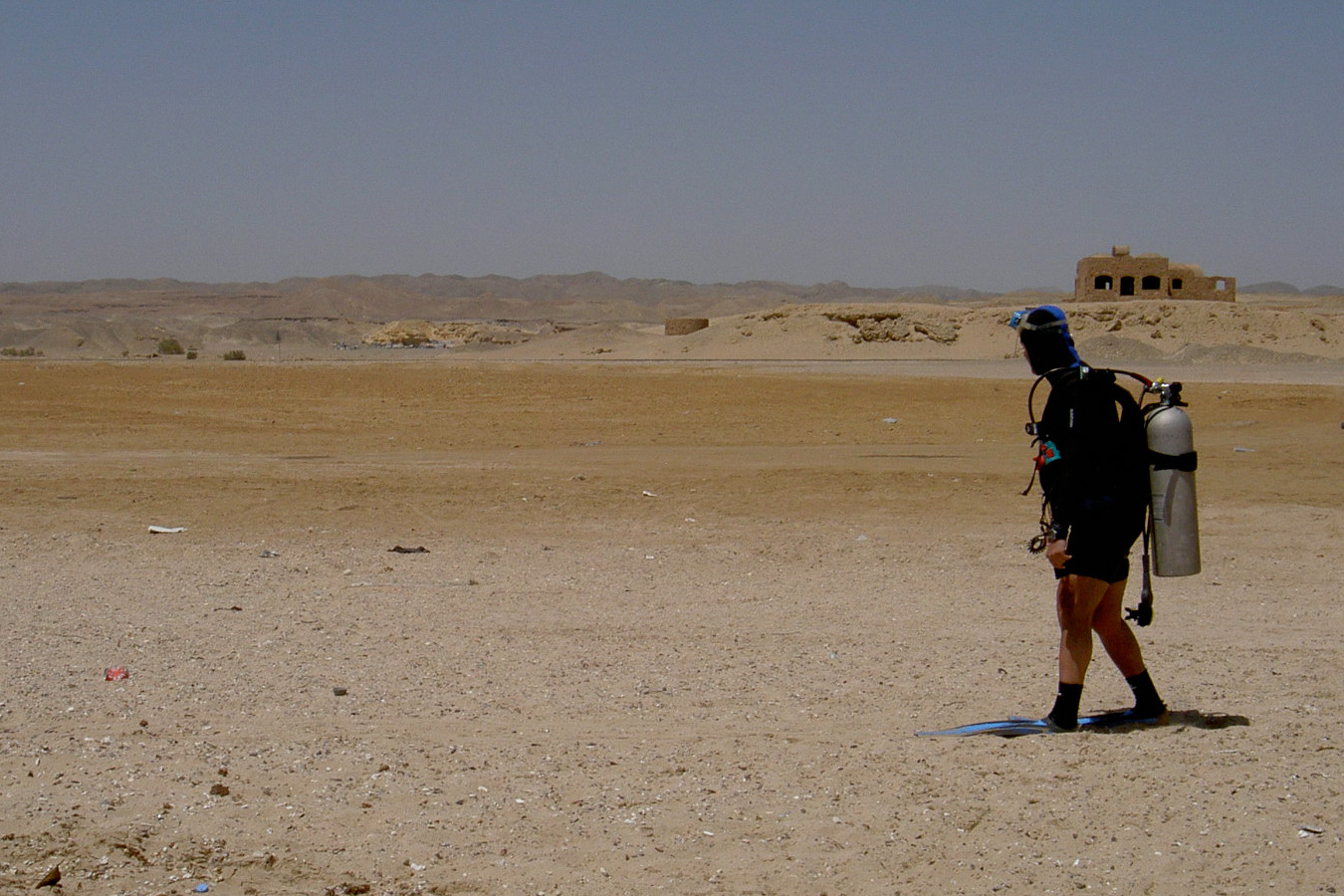 Photo d'un plongeur en combinaison néoprène et avec des bouteilles de plongée sur le dos… en train de marcher dans le désert