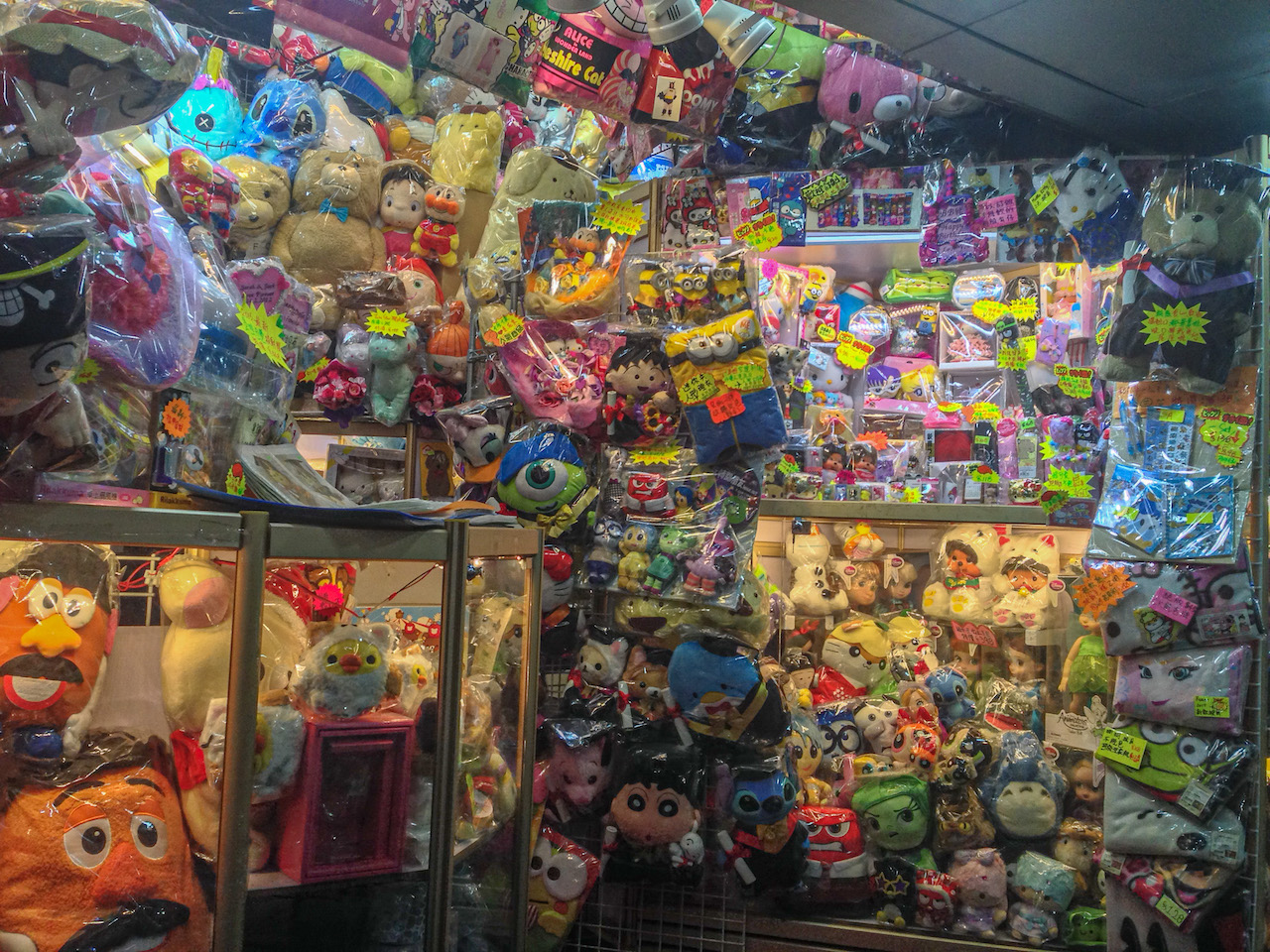 Photo de l'intérieur d'une toute petite boutique avec des peluches colorées  du sol au plafond, emballées dans des sachets plastique ou sous vitrine.