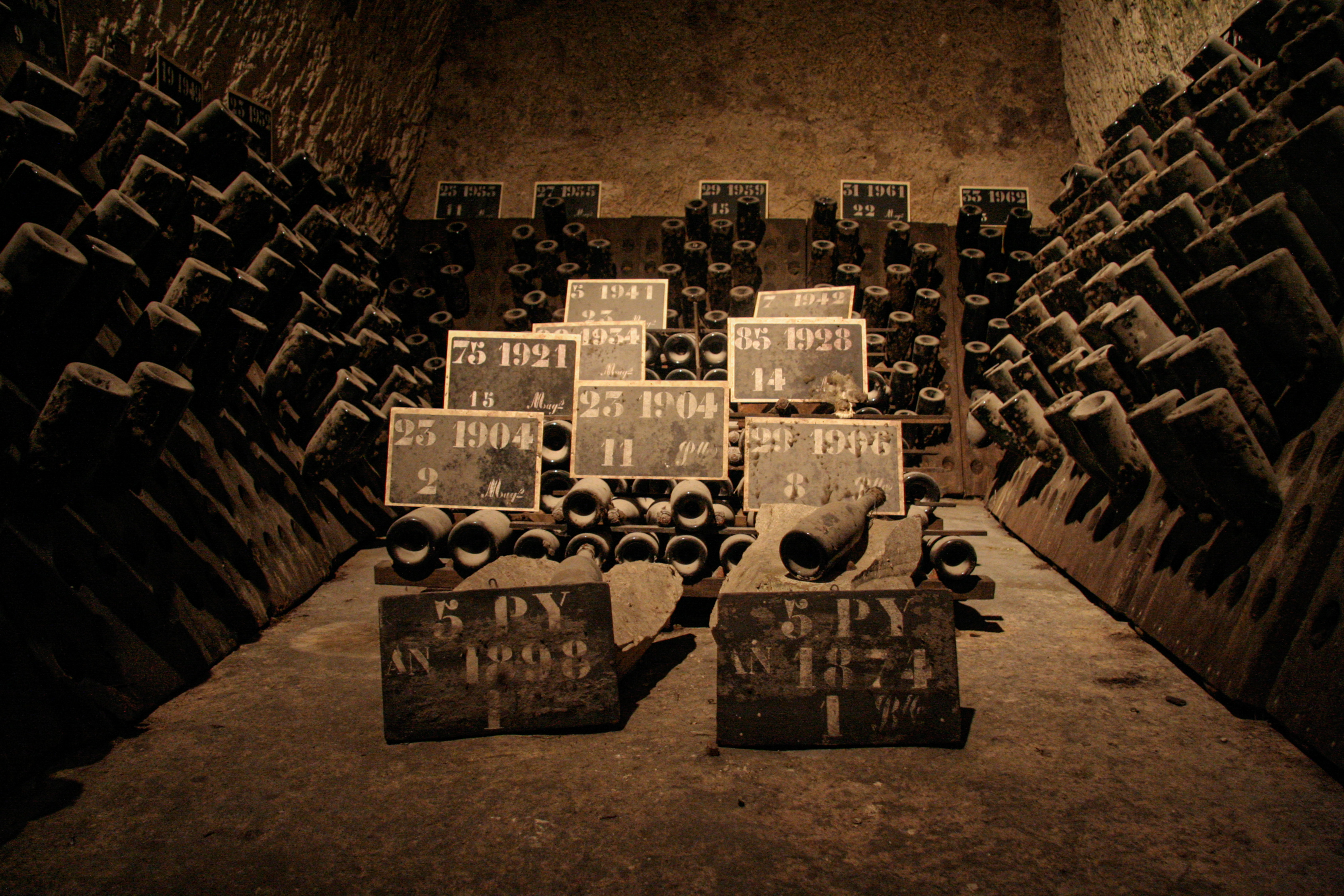 Photo of multiple bottles of wine full of dust, in a cellar.