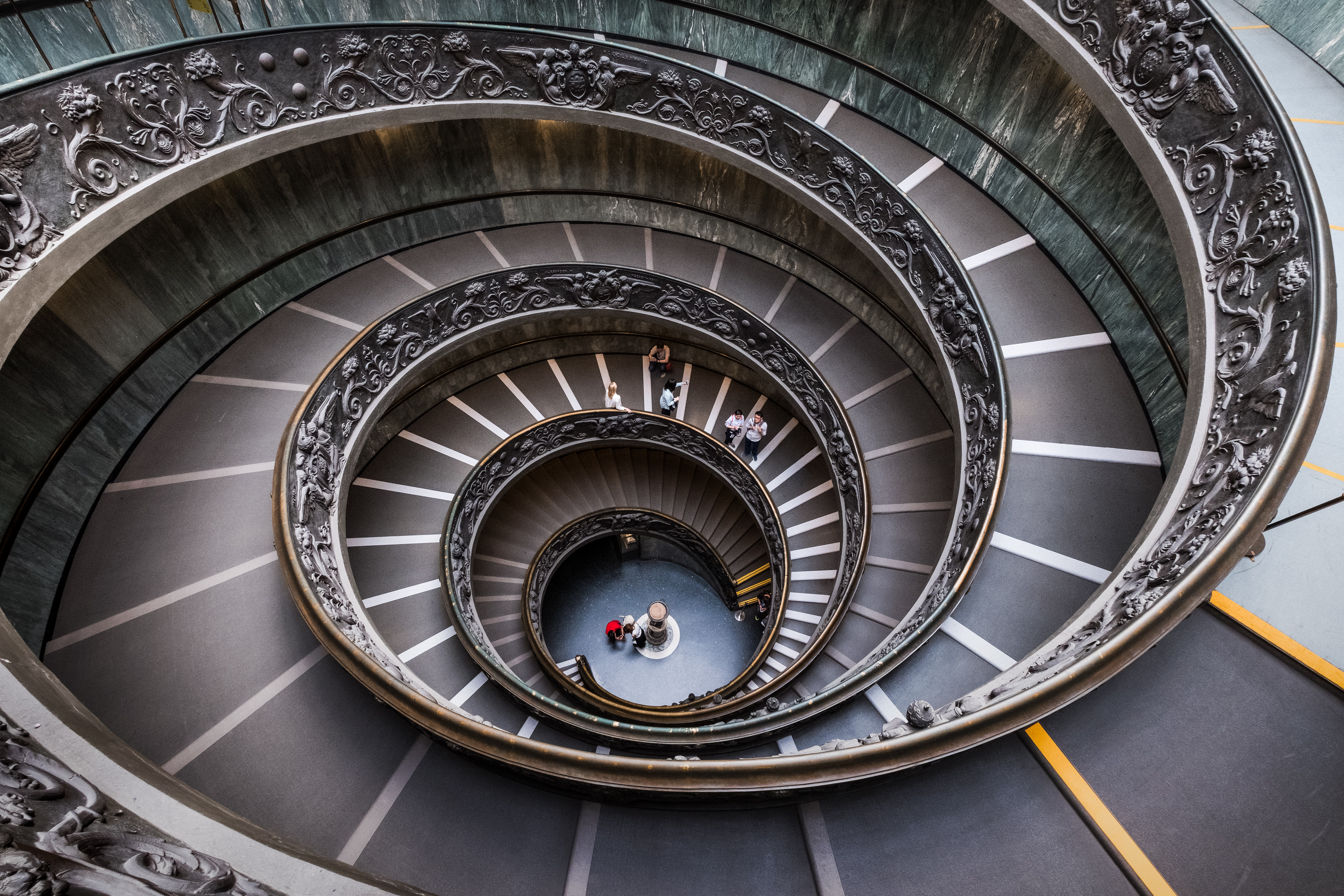 Plunging photo of a wide staircase in double helix, with some people