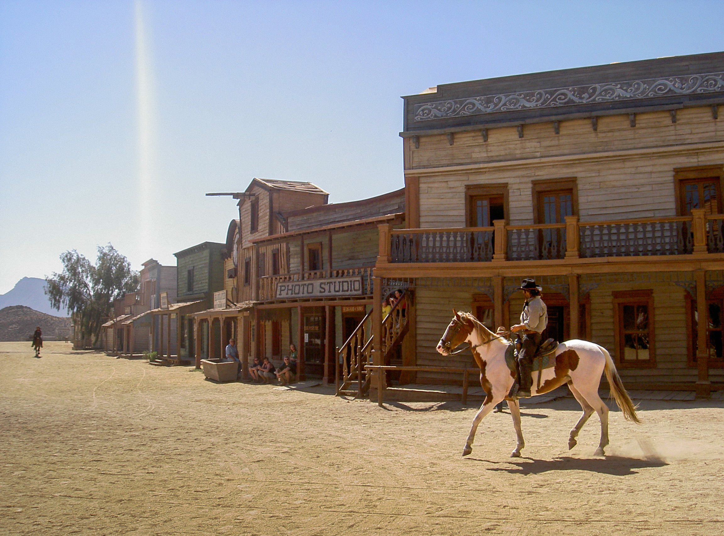 Photo of a person riding a horse in a Western-style town (a movie studio)) with historic buildings, including a photo studio.