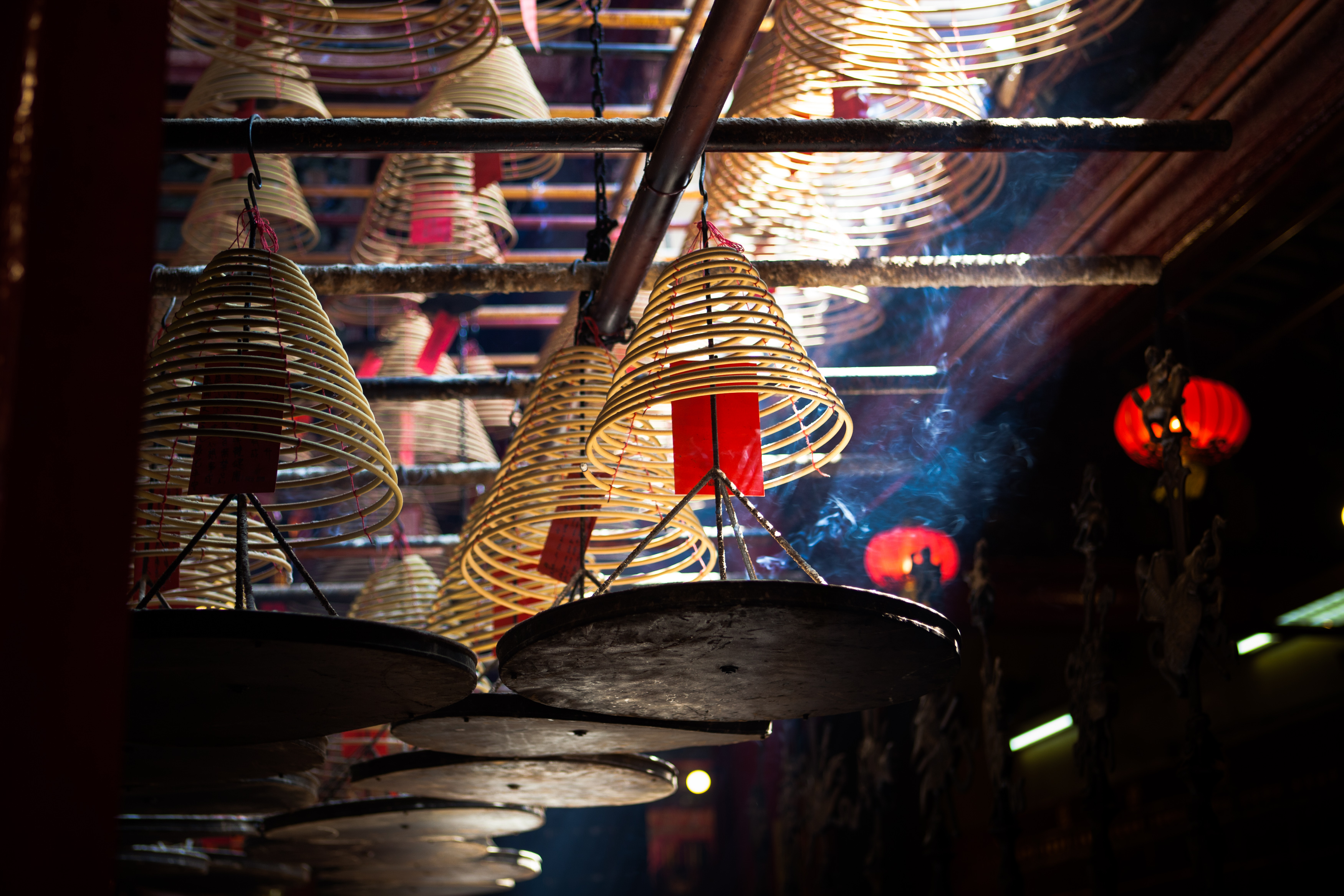 Photo of smoking incense spirals, hanging from the ceiling of a temple, with a light beam in the darkness