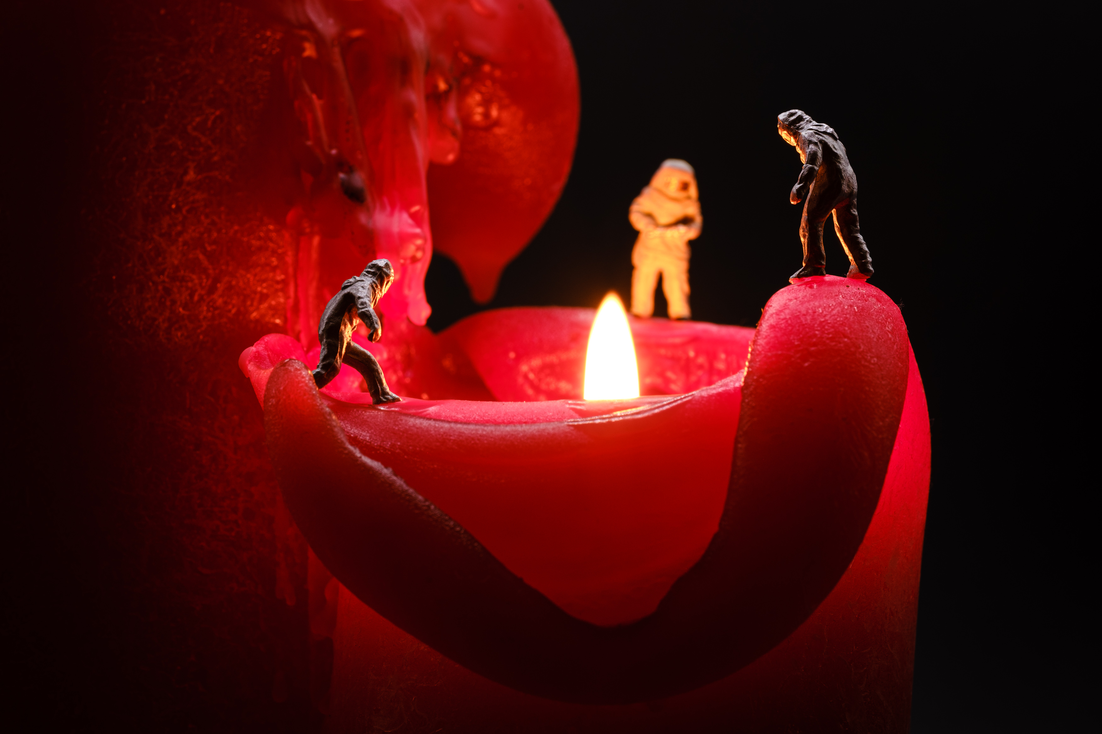 Macro photo of a lit red candle and small miniature figures of volcanologists on the edges (scale 1/87th)