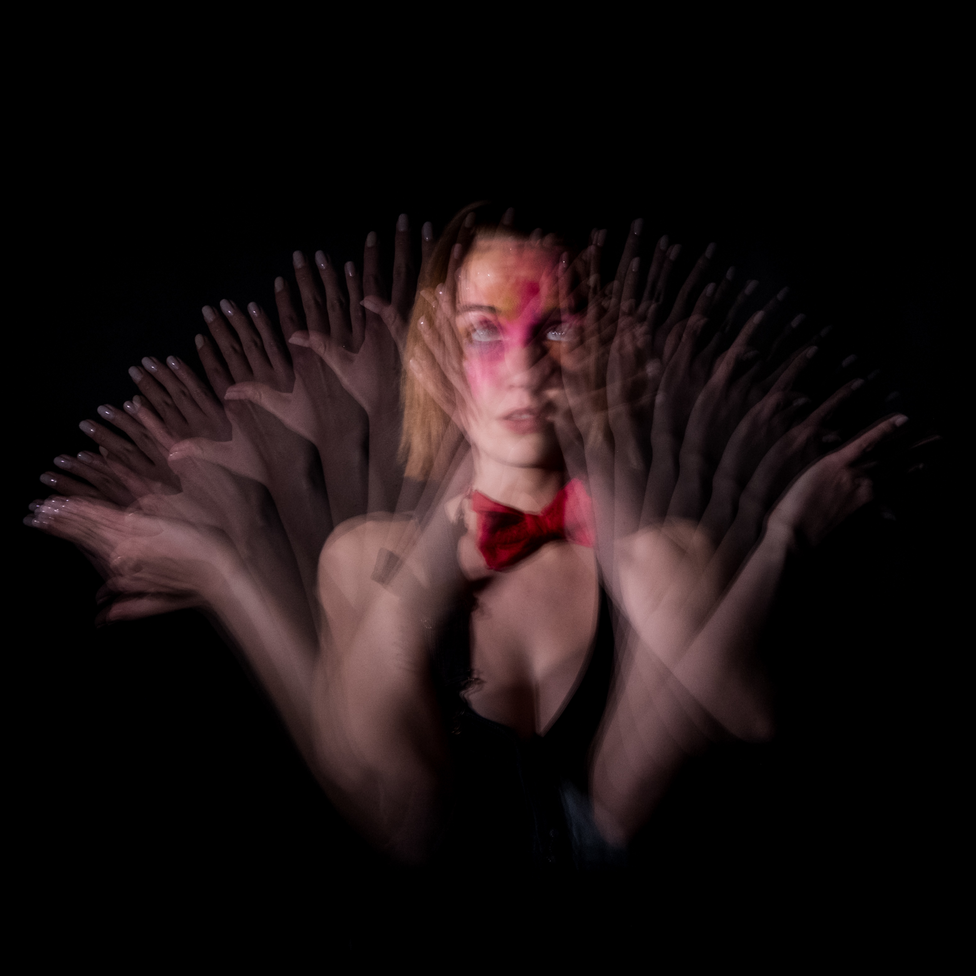 Bust picture of a young woman moving back and forth with her arms, visible in several places thanks to the light of a stroboscope.