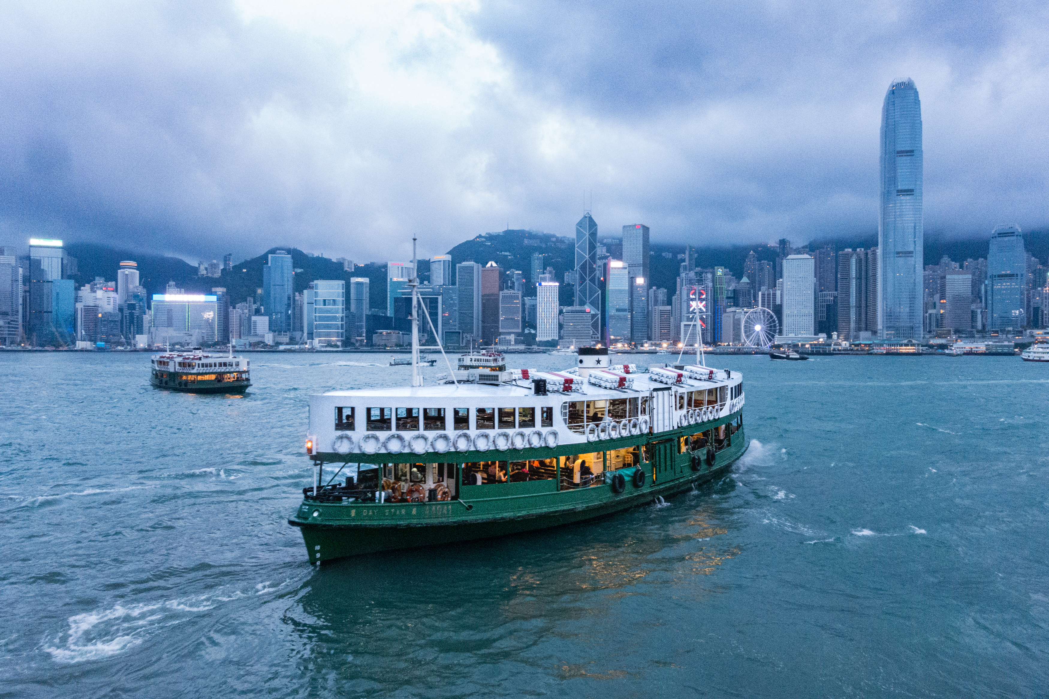 Photo of an old green and white boat on the sea in Victoria Harbour in Hong Kong, with many buildings in the background